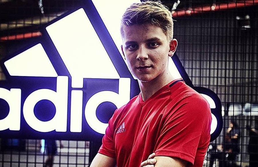 Youtuber Till Schüttrumpf steht mit verschränkten Armen vor einem adidas-Logo.