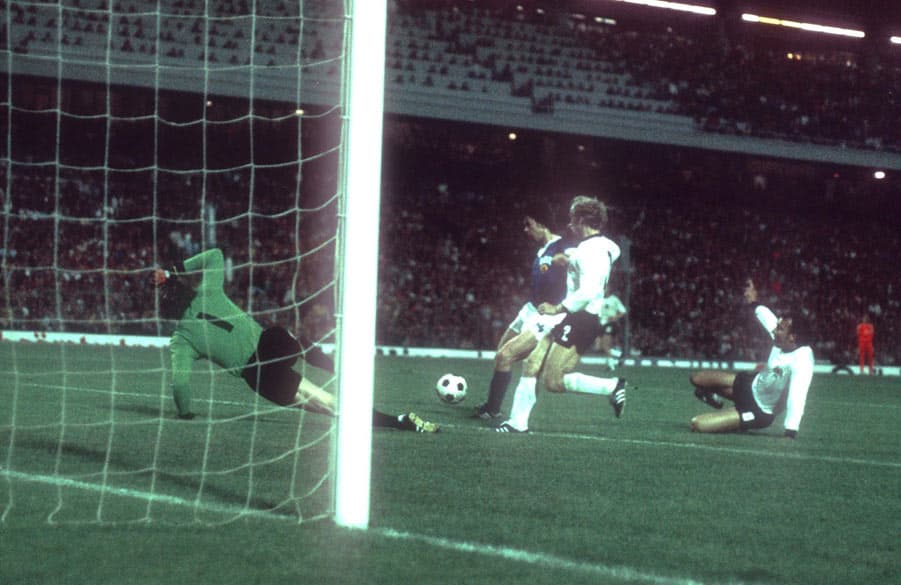 Jürgen Sparwasser pushes past defender Berti Vogts as goalkeeper Sepp Maier looks on.