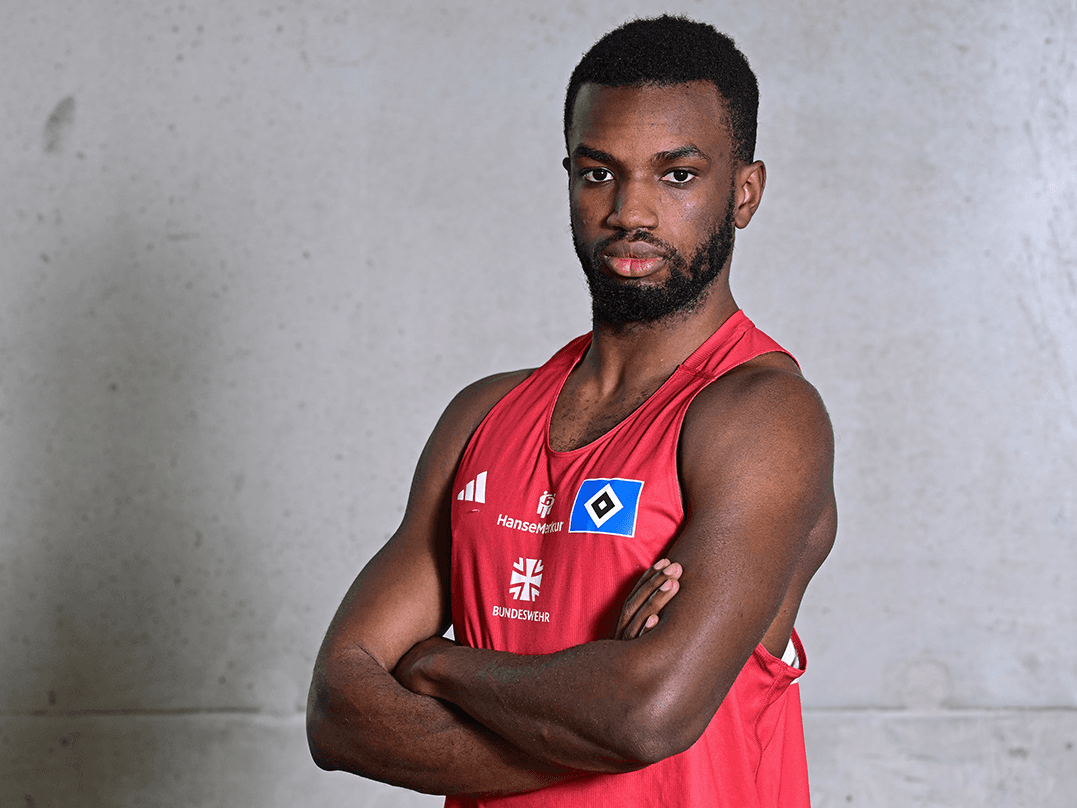 A person in a red sports jersey with crossed arms, standing against a plain background.