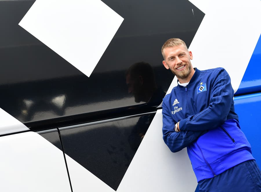 Aaron Hunt lehnt an einer Mauer, die die HSV-Raute trägt.