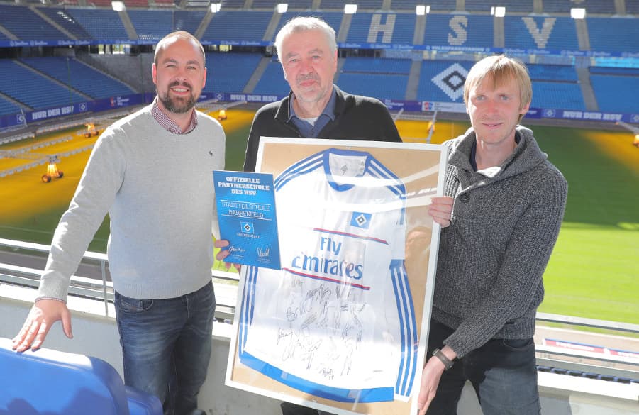 Schulkoordinator Matthias Hellmig (l.) präsentiert gemeinsam mit Sebastian Schmidt und Gerd Thiem von der Stadtteilschule Bahrenfeld Urkunde und Trikot.