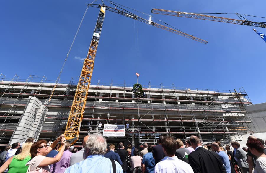 Der Kranz zum Richtfest wird von einem Kran vor dem Gebäude hoch gehalten.