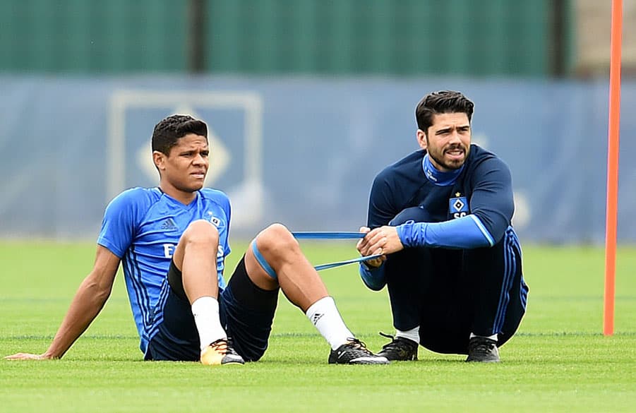 Douglas Santos sitzt mit Reha-Trainer Sebastian Capel auf dem Rasen.