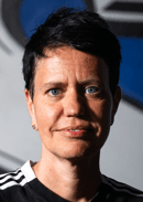 Fanny Boys. A person with short dark hair and blue eyes, wearing a black and white sports shirt, posing against a blurred backdrop with blue and gray elements.