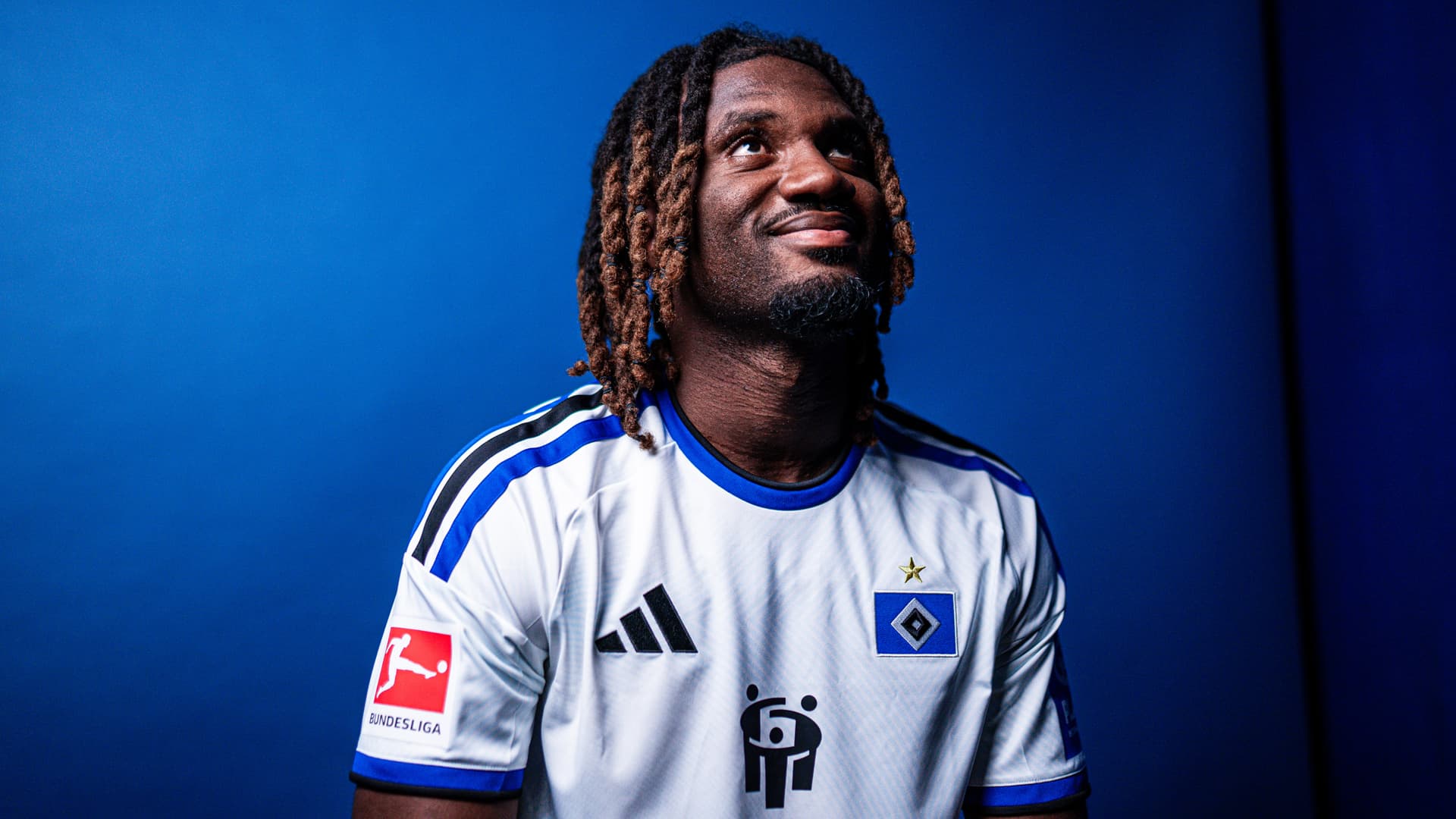 Sommer-Zugang Terem Moffi im HSV-Trikot bei seinem Vorstellungsshooting. Er blickt nach oben und lächelt.
