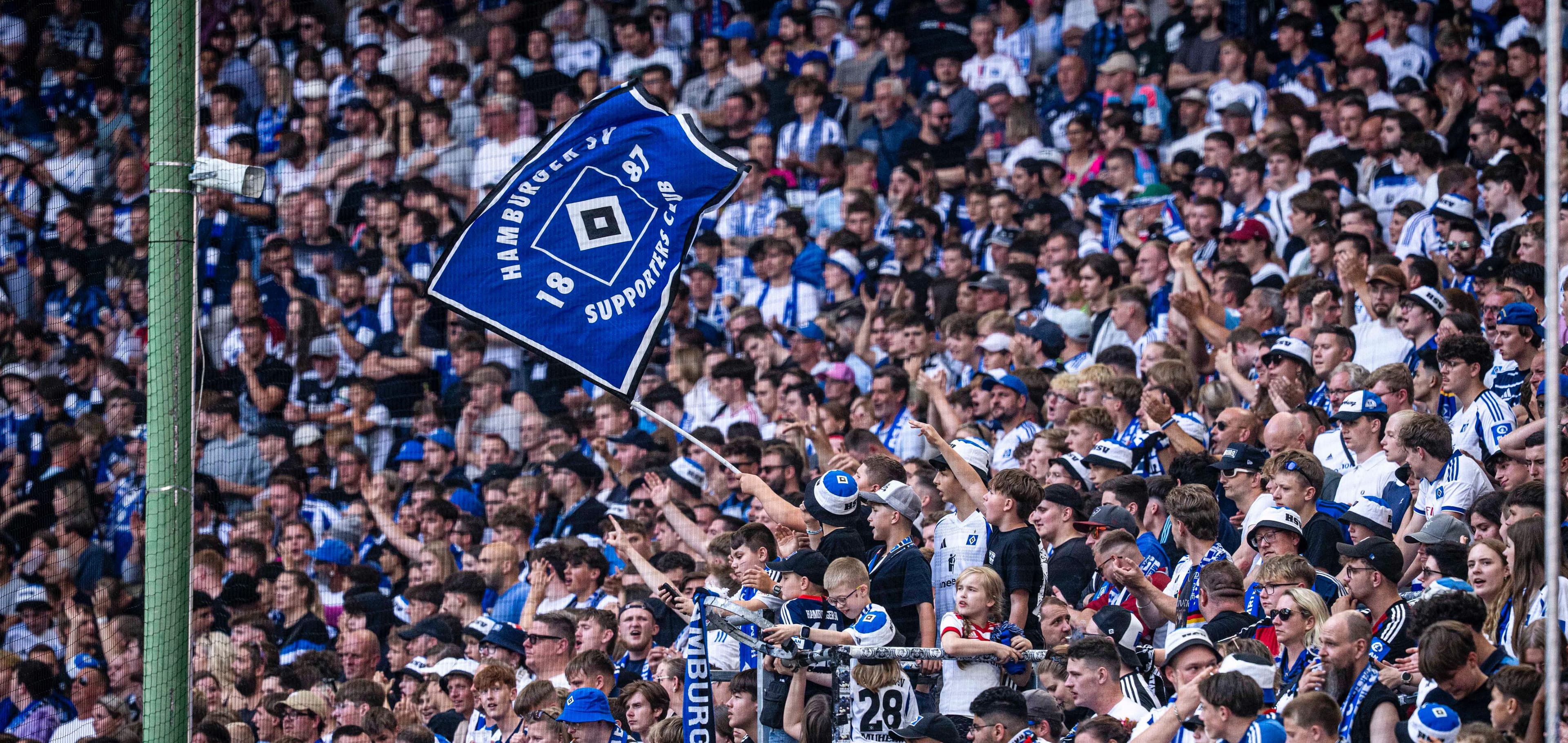 Crowd of enthusiastic football fans celebrating in a stadium, waving blue and white flags and wearing team colors.