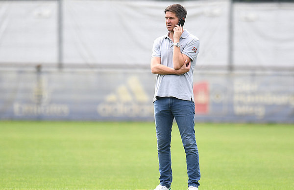 Ralf Becker steht mit Telefon am Trainingsplatz.