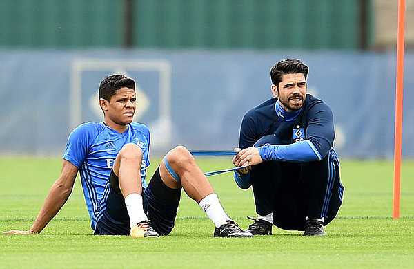 Douglas Santos sitzt mit Reha-Trainer Sebastian Capel auf dem Rasen. 