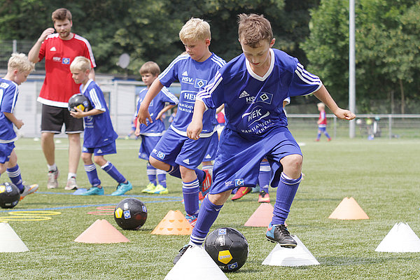 In den HSV-Fußballcamps erhalten die Kinder und Jugendlichen fachspezifische Trainingseinheiten und haben zudem Spaß dabei. Junge Fußballer spielen den Ball im Slalom um die Pylonen.
