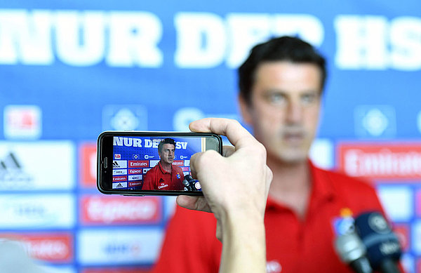Jens Todt wird vor einer Sponsorenwand von einem Handy gefilmt. 