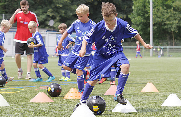 Fußballschulen-Teilnehmer dribbelt um Hütchen.