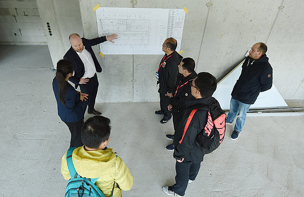 Die Delegation aus China steht auf der Campus-Baustelle. 