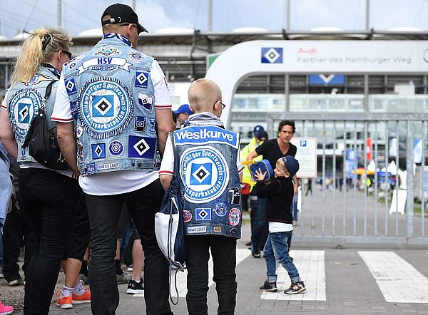 Der Familienname der meisten Mitglieder ist Schmidt. Der häufigste Vorname ist Michael. Und der Durchschnittsfan ist ca. 50 Jahre alt. Ein Mann, eine Frau und ein Kind stehen mit Kutten vor dem Volksparkstadion.