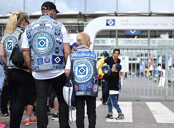 Ein Mann, eine Frau und ein Kind stehen mit Kutten vor dem Volksparkstadion.