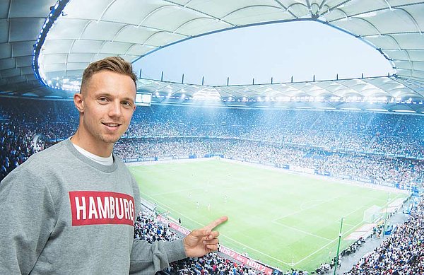 Sonny Kittel steht vor einem Bild des Volksparkstadions und zeigt darauf. 