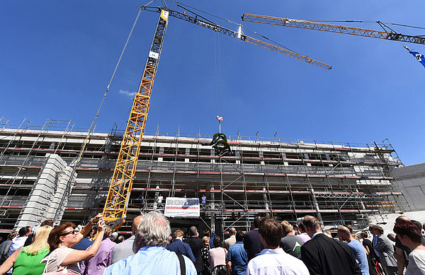 Ein Kran hält den Richtfest-Kranz vor der Baustelle.