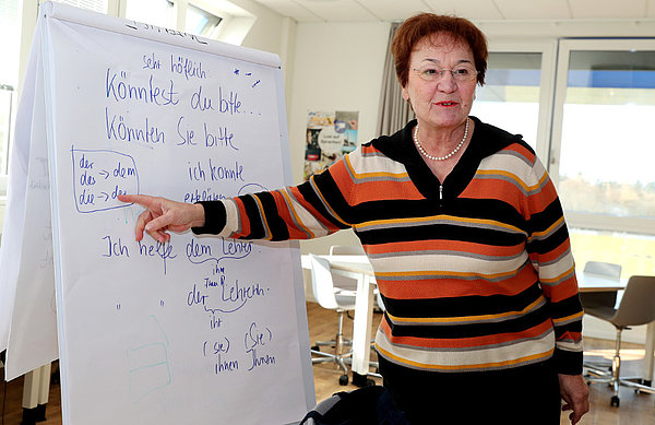 „Es heißt, ich helfe dem Lehrer.“ Vesna erklärt ihren Schülern, welcher Artikel in den Satz gehört. Frau Vesna zeigt auf einen Aufsteller mit Sätzen.