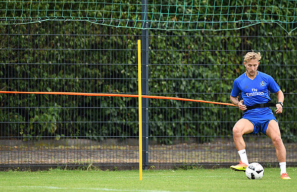 Lewis Holtby passt einen Ball zurück. Um seine Hüfte ist ein Band geschnallt, dass am Zaun befestigt ist.