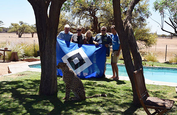 Die HSV-Fans in Namibia posieren mit HSV-Flagge und einem Geparden im Vordergrund.